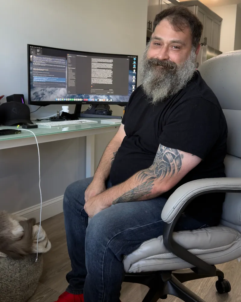 Greg working at his desk at home with a cat asleep beside him