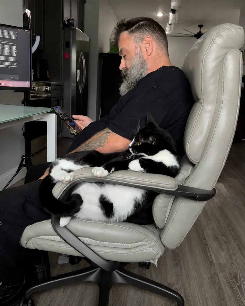 Greg at his desk with the cat Skinwalker Texas Ranger draped over the chair.