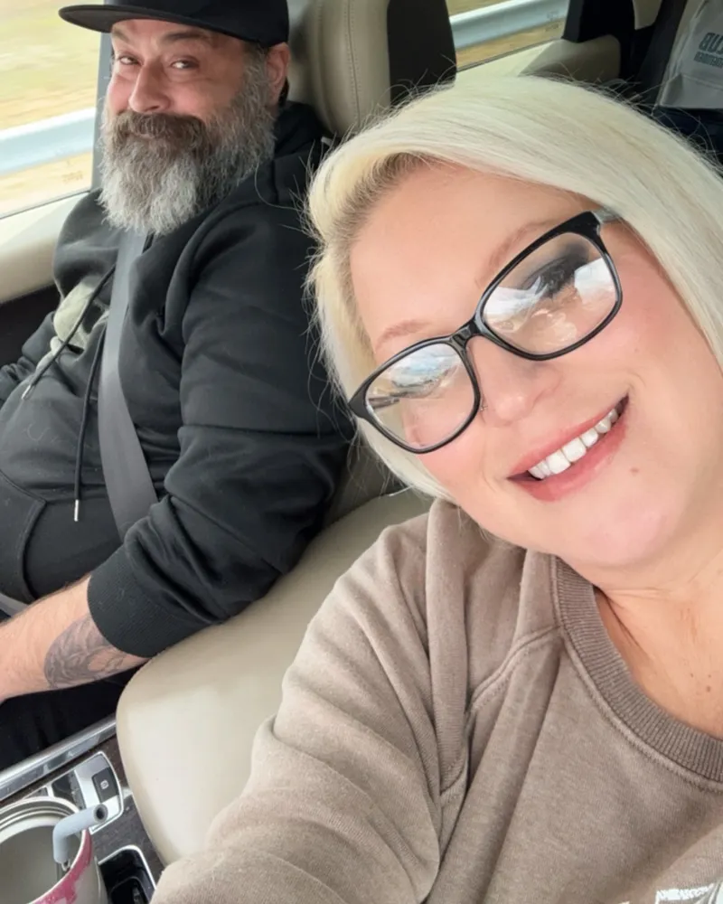 Greg driving and Nerissa riding shotgun, both smiling in the front seat.