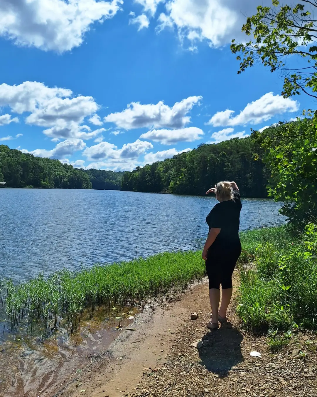 Nerissa standing at the edge of a lake on a bright summer day, looking out over the water.