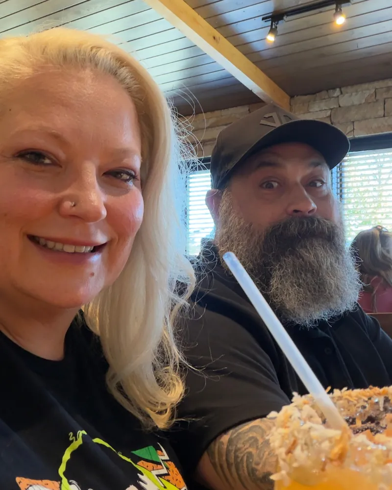 Nerissa smiling at Cheddar's with a frozen coconut drink while Greg stares wide-eyed at the camera beside her.