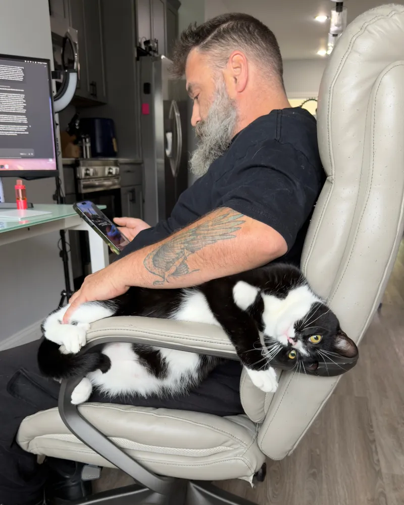 Greg at his desk answering messages with the family cat stretched out beside him.