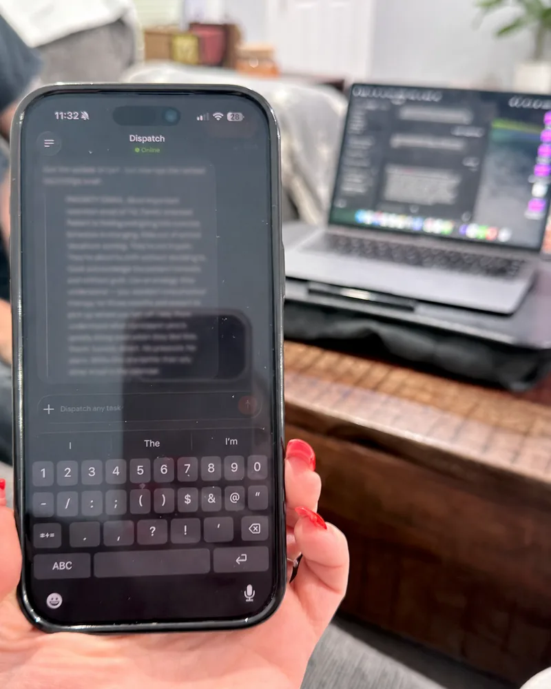 Nerissa holding an iPhone running an AI agent chat late at night, with her MacBook open to code on a lap desk behind it.
